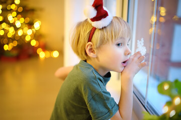 Little excited child is waiting Santa Claus on Christmas Eve. Preschooler boy looking on window and hope of magic and gifts at New Year night.