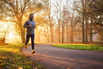 Poster Adult male runner in park at autumn sunrise © baranq