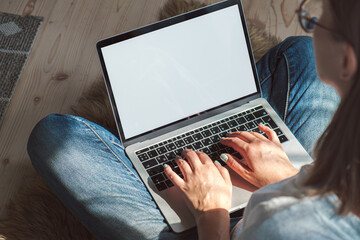 Young woman using laptop blank screen to work, sitting on the fl