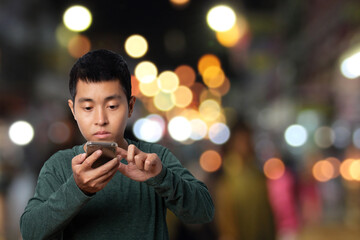 Young man using smartphone with abstract blur of a night market background.
