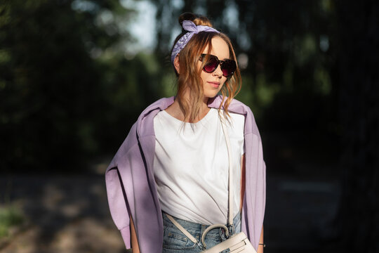 Pretty young hipster woman with fashion sunglasses and a bandana with a purple hoodie walks on the street