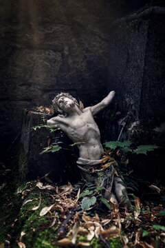 a small broken statue of Jesus Christ on a decayed grave