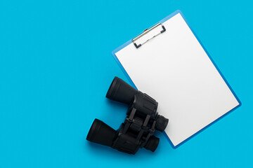 Clipboard with a blank sheet and binoculars on a blue background. Hiring concept, help wanted. Banner. Flat lay, top view