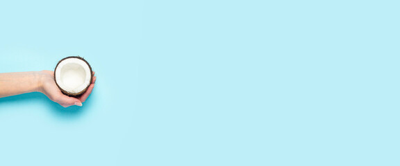 A woman's palm holds an open half of a coconut on a blue background. Top view, flat lay. Banner
