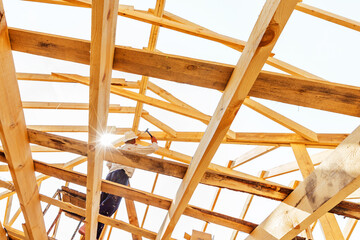 Construction of a wooden roof. The constructed structure of beams and partitions against the background of the builder fixing the details of the structure. Foreground. Selective focus