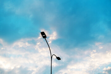 Lamp post against the background of the cloudy sky. Urban street lighting system with double lamps....
