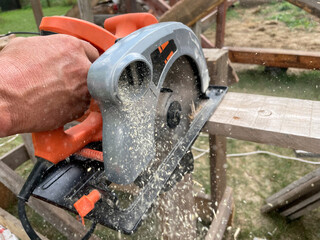 Milling wood in the joinery using manual mechanical cutters. Hands of a man who is sawing a tree with a circular saw. Flying sawdust in the air. 