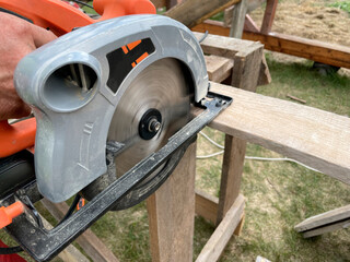 Milling wood in the joinery using manual mechanical cutters. Hands of a man who is sawing a tree with a circular saw. Flying sawdust in the air. 