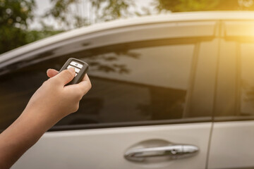 Young woman holding and pushing a car remote control to lock or unlock the car.