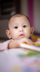 Fototapeta premium Baby Asian Girl peaking over table as she practices to stand devloping motor skills