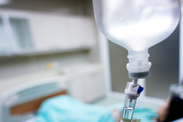 Close up Infusion bottle pump with saline solution drip and clipping path for patient admit room in hospital. Patient is waiting for doctor on bed preparing for surgery or diagnose in green dress.