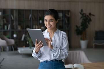 Smiling Indian young woman use modern tablet gadget talk speak on video call. Happy mixed race...