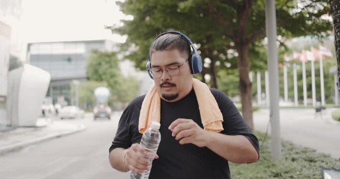 Obesity Asian man Drinking mineral water after running in park morning. Jogging workout to burn body fat to healthy. Commitment to body care for good health. Weekend activity happy lifestyle concept.
