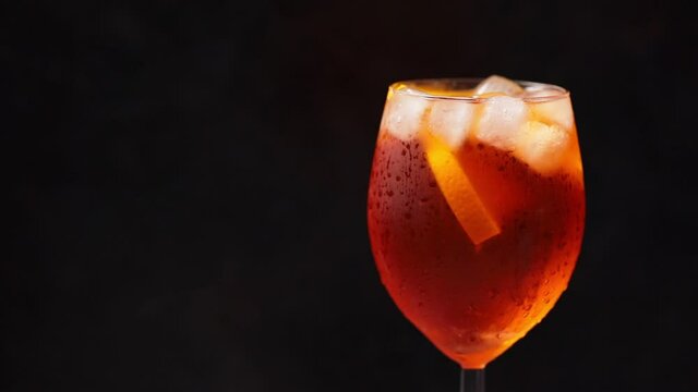 Cocktail aperol spritz rotates on black background. Summer orange cocktail in a rotating glass. Rotate. Copy space