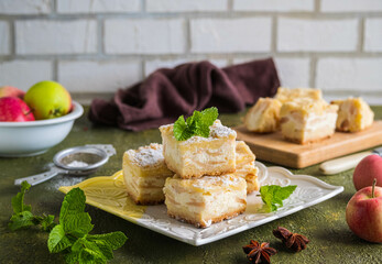 Sliced apple pie made from shortcrust pastry with cottage cheese cream and apple wedges on a square plate on a green concrete background. Apple pie recipes.