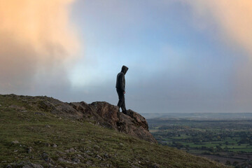 A mysterious hooded figure. Standing on top of a hill, Looking out across the countryside.