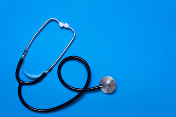 Black stethoscope isolated on blue background with copy space.