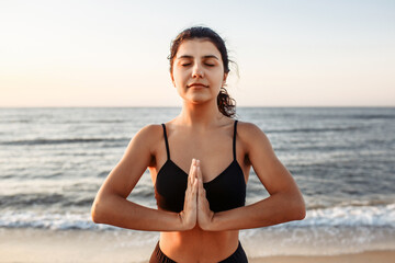 Fototapeta na wymiar Close up shot of a woman with closed eyes practicing yoga at the beach on the sunset. A woman in sportswear goes in for sports or fitness.