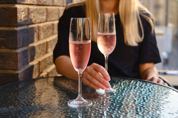 A glass of rose wine in the hands of a girl relaxing on restaurant terrace. Summer holiday. Celebrate and enjoy moment. Alcoholic drink tasting. Romantic evening aperitif. Wine glass closeup