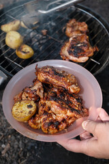 Cooking chicken on a barbecue with charcoal in the garden. Grilled chicken thighs with potato slices. Natural cuisine. Vertical orientation