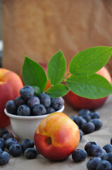 Peaches and blueberries are served on a white plate.
Soft fresh summer blueberry, peach and green berry leaves on craft paper.