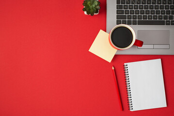 Overhead photo of laptop plant cup of coffee notepad sticker and pencil isolated on the red...
