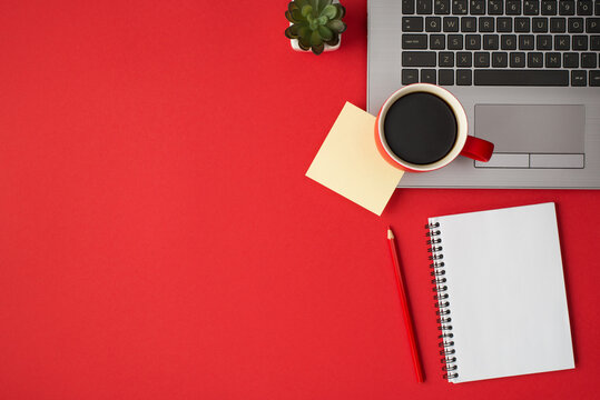 Overhead photo of laptop plant cup of coffee notepad sticker and pencil isolated on the red backdrop with blank space - Powered by Adobe