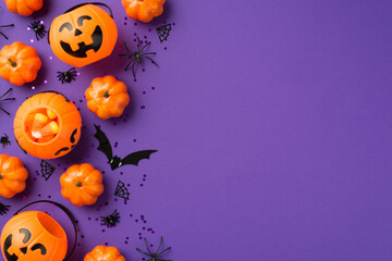 Top view photo of halloween decorations pumpkin baskets candy corn black sequins spiders web and bat silhouette on isolated violet background with copyspace