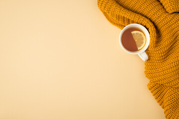 Top view photo of yellow knitted sweater and cup of tea with lemon slice on isolated pastel orange background with copyspace