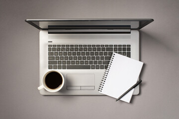 Top view photo of cup of coffee pen and open spiral copybook on grey laptop on isolated grey background with copyspace