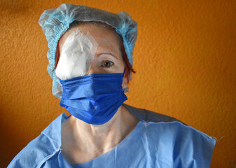 Woman operated on the right eye, wears a disposable gown and a disposable cap, brings the eye...
