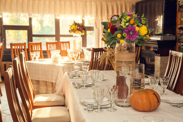Festive floristry in autumn style with numbering of tables on pumpkins in banquet hall.