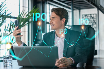 Businessman in suit using smart phone to optimize IPO strategy at corporate finance. Chart hologram over modern panoramic office background