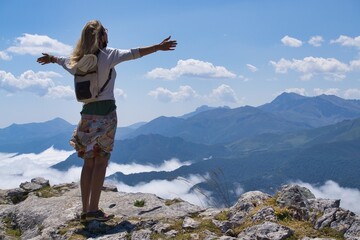 Naklejka premium Senior woman on top of a mountain spreads her arms wide in admiration of the landscape