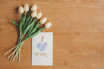 Top view of lovely greeting card I love mom and flowers on wooden background