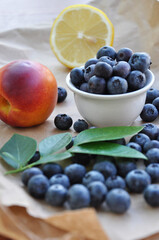 Peaches and blueberries are served on a white plate.
Soft fresh summer berries and leaves of blueberries, peaches and green berries on craft paper.