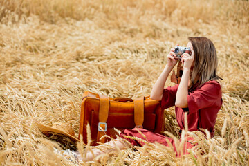 young woman in red dress with camera and suitcase on wheat field