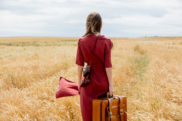 young woman in red dress with camera and suitcase on wheat field