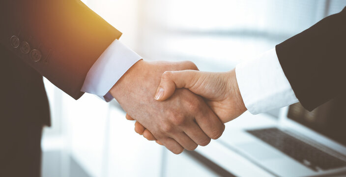 Businessman and woman shaking hands in sunny office, close-up. Concept of handshake as success symbol in business