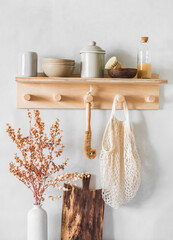 Simple kitchen - a wooden shelf with bowls, with a brush for washing dishes, detergent, dried flowers, a cutting board on a light background