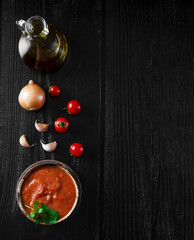 Authentic Spanish Sofrito sauce made with tomato, peppers, onion, garlic, herbs and olive oil in glass jar. Dark wooden background, to view with copy space