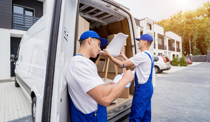 Two removal company workers are loading boxes and furniture into a minibus. © romaset