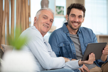 pleasant young man showing tablet to his elderly father