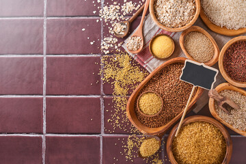 White, brown and red rice, buckwheat, millet, corn groats, quinoa and bulgur in wooden bowls on a brown stone kitchen table. Gluten-free cereals. Top view with copyspace