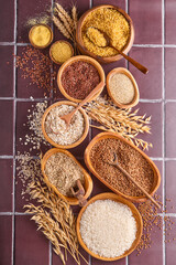 White, brown and red rice, buckwheat, millet, corn groats, quinoa and bulgur in wooden bowls on a brown stone kitchen table. Gluten-free cereals. Top view with copyspace