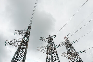 Power line pylons with high voltage wires against a cloudy sky background