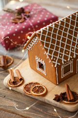 Christmas. Homemade gingerbread house, presents wrapped, spices, dry slices of orange as decor. Cozy home atmosphere, family time. Natural rustic elements, zero waste concept, eco-friendly. Close up