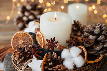 Rustic decor for christmas holiday family dinner. Center piece with white candle, dry orange, cones, cotton. Zero waste eco friendly home decoration. Cozy atmosphere, wooden background. Close up