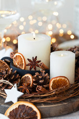 Fototapeta na wymiar Rustic decor for christmas holiday family dinner. Center piece with white candle, dry orange, cones, cotton. Zero waste eco friendly home decoration. Cozy atmosphere, wooden background. Close up