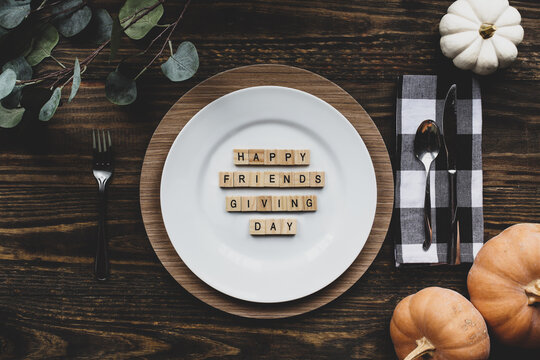 Thanksgiving Place Setting With Plate, Napkin, On A  Decorated Table Shot From Flat Lay Or Top View Position. Happy Friendsgiving Day Spelled Out With Wood Block Letters.